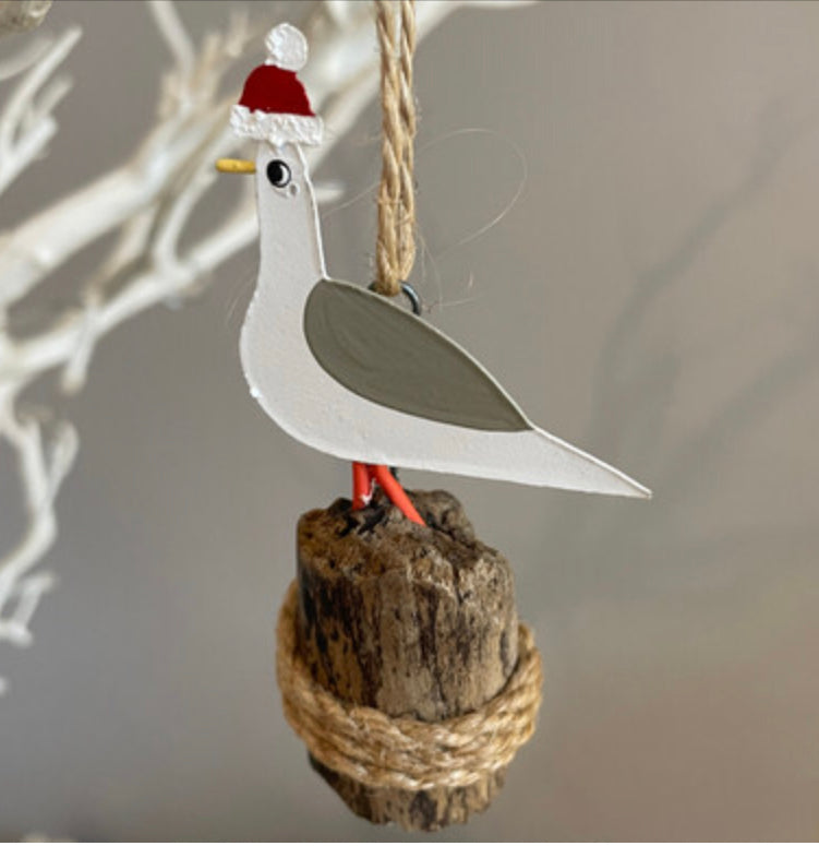 Seagull in bobble hat on groyne hanging Christmas decoration by Shoeless Joe