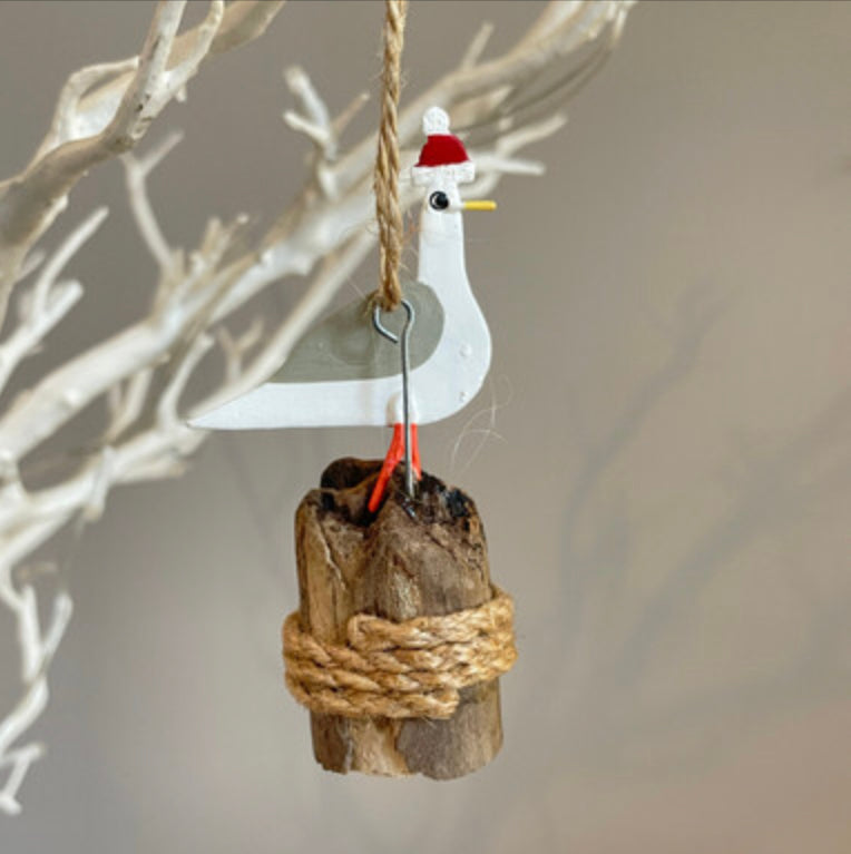 Seagull in bobble hat on groyne hanging Christmas decoration by Shoeless Joe